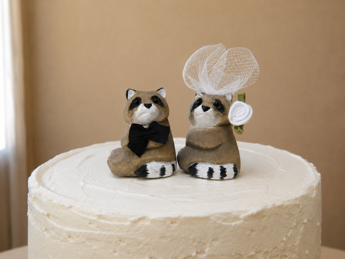Raccoon hand-carved wooden cake topper by Selsela, bride and groom pair on a wedding cake