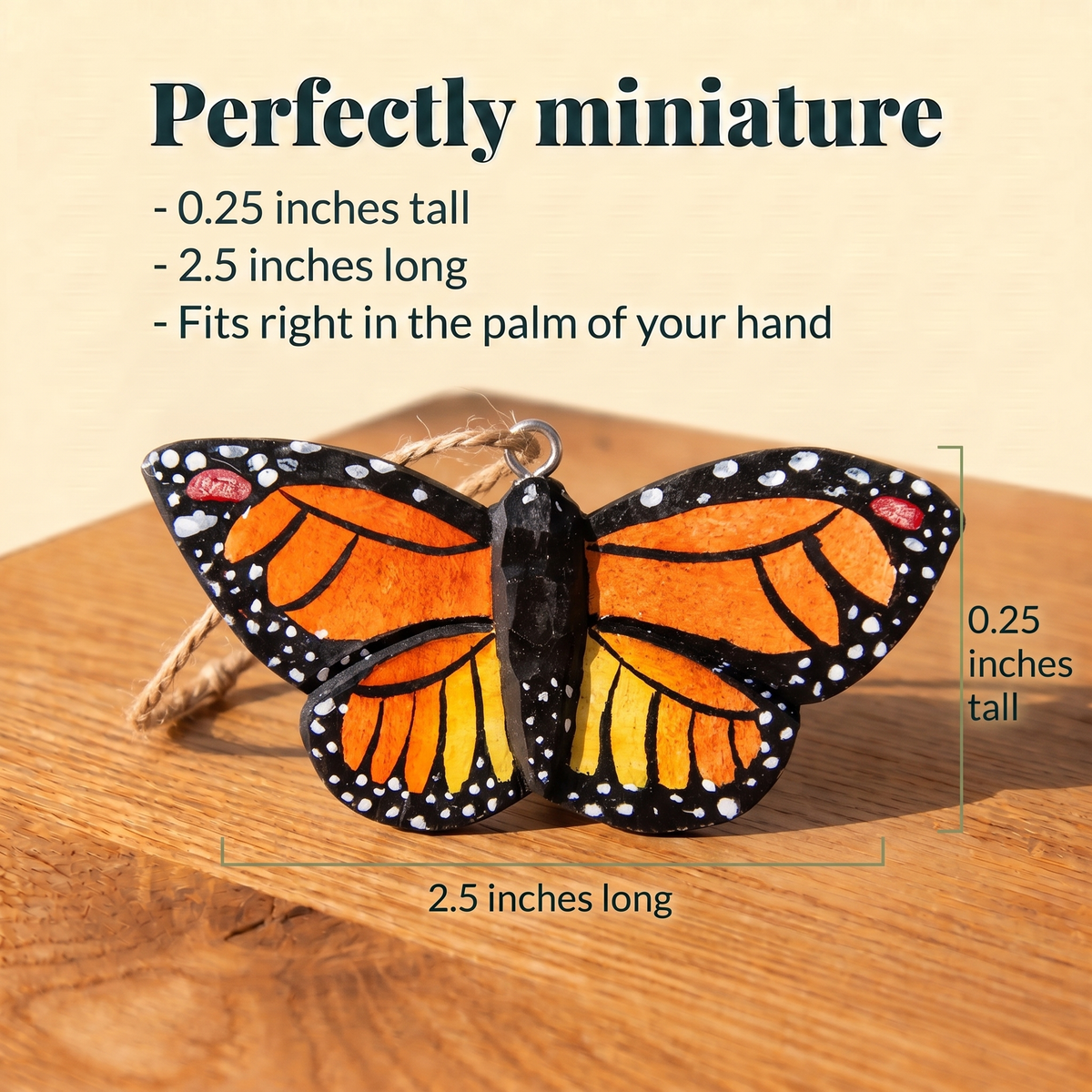 Wooden Monarch Butterfly ornament with a twine loop on a sunlit wood table, measured at 0.25 inches tall and 2.5 inches long. Text reads: Perfectly miniature, fits right in the palm of your hand.