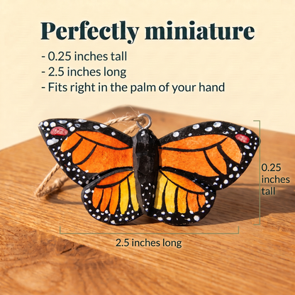 Wooden Monarch Butterfly ornament with a twine loop on a sunlit wood table, measured at 0.25 inches tall and 2.5 inches long. Text reads: Perfectly miniature, fits right in the palm of your hand.