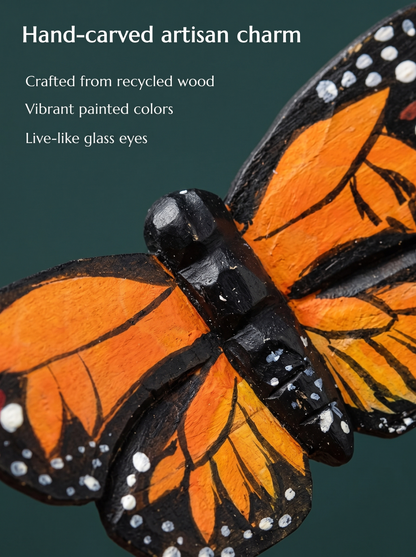 Close-up of the carved Monarch Butterfly body and wings with orange panels, black veins and white dotted borders. Text reads: Hand-carved artisan charm, crafted from recycled wood, vibrant painted colors, live-like glass eyes.